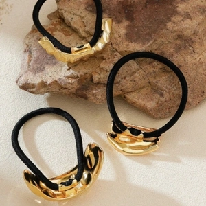Three irregular gold metal ponytail holders with black elastic bands on stone background