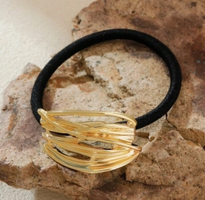 Detail of a wavy gold metal accent on a black elastic hair tie set on a natural stone surface