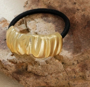 Detail of golden wavy textured metal ornament on black elastic ponytail holder