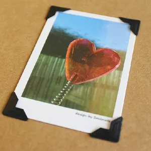 Macro detail of black adhesive photo corners securing a heart card on kraft paper