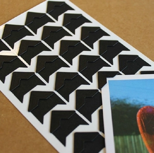 Detail showing a black triangular photo corner sticker being applied to secure a photograph