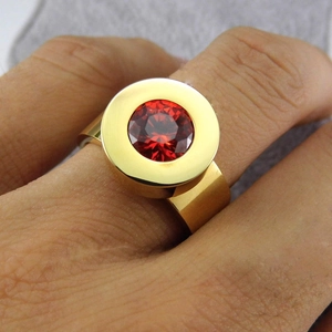 Close-up of a wide 18K gold-plated ring featuring a large round red zircon gemstone inlay