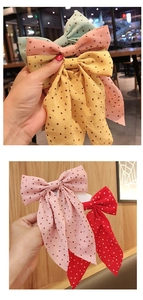 Detailed view of handmade polka dot bow hair clip with flowing ribbons held in hand