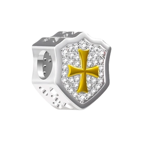 Macro shot of silver and gold shield charm with cross pattern and inset crystals