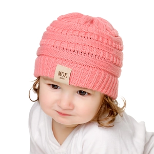 Detailed close-up of a pink knitted baby hat featuring a MOK KIDS woven fabric label