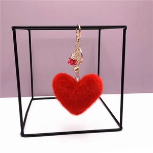 Plush red heart keychain with gold ring and tassel on a modern geometric stand