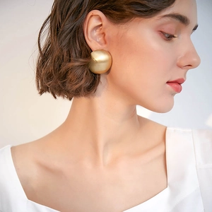 Close-up of model wearing large matte golden sphere earrings in vintage French style