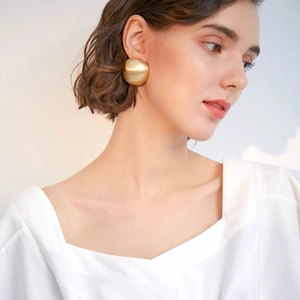 Model wearing gold matte spherical geometric stud earrings with brushed metallic finish