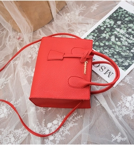 Detailed close-up of a red litchi texture handbag with gold logo and lace background