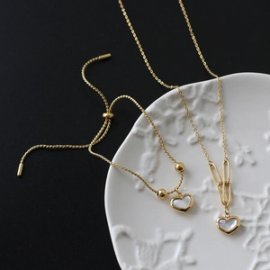 Macro detail of heart-shaped shell pendant on gold paperclip chain and bracelet
