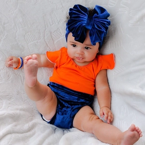 Close-up of baby set with orange ruffle top, blue velvet shorts, and matching bow headband
