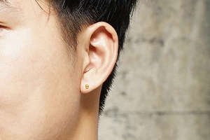 Gros plan d'un clou d'oreille sphérique minimaliste en or sur le lobe d'une oreille