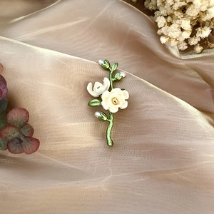 Detail of white enamel camellia brooch with green leaves and freshwater pearl on silk