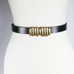 Detail of slim black leather belt featuring a segmented gold caterpillar buckle on model