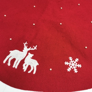 Close-up of red knit Christmas tree skirt with white deer embroidery and pearl accents