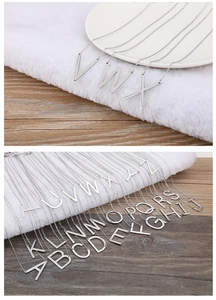 Detailed view of silver titanium steel alphabet pendants A-Z on a soft velvet surface