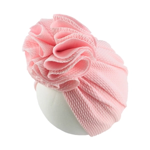 Side view of baby pink waffle knit turban hat with large ruffled flower on white display