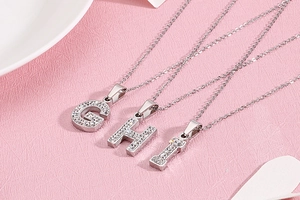 Détail de pendentifs lettres G, H, I en argent pavés de cristaux de zircone scintillants
