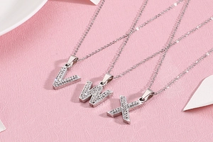 Détail de pendentifs lettres V W X argentés avec strass pavés sur des chaînes fines