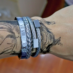 Close-up of men's silver stainless steel Roman numeral cuff and braided wire bracelets