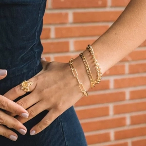 Detail showing stacked gold paperclip, figaro, and cuban chain bracelets on wrist