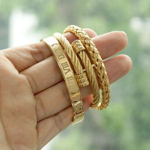 Detail of three-piece gold-plated crown and roman numeral bracelets on a hand