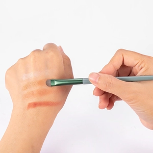 Flat eyeshadow brush detail showing warm color pigment swatches on skin surface