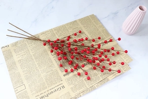 Detailed macro view of three artificial red berry branches on a vintage newspaper background