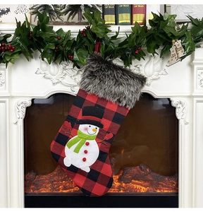Detail of a red and black buffalo plaid Christmas stocking with a snowman on a mantel