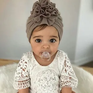 Detailed close-up of a tan baby turban hat with a large layered flower on an infant