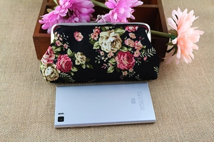 Close-up of floral fabric wallet with rose patterns and metal clasp next to a phone