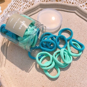 Detail of high-elastic seamless hair ties in green shades inside a clear storage jar