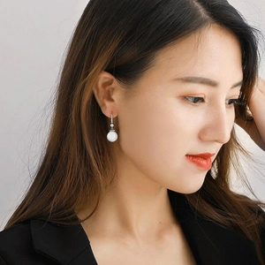 Detail of elegant pearl drop earrings with sparkling crystals worn by a model in a black suit