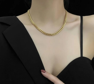 Collier chaîne Cuban épaisse en acier inoxydable doré porté par un mannequin sur fond sombre