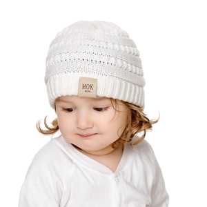 Detail view of the soft white knit baby hat featuring a branded MOK leather patch on front