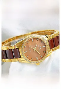 Detail of a gold watch with coffee ceramic links and a sparkling rhinestone bezel