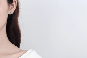 Detailed view of silver bow-shaped stud earrings with blue moissanite on a model ear
