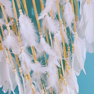 Detailed view of white feathers, wooden beads, and ribbons on a large dreamcatcher