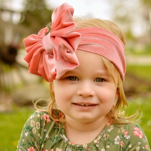Outdoor shot of a baby girl wearing a large pink velvet bow headband with soft grass background