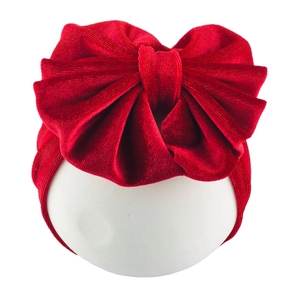 Close-up of bright red velvet oversized bow headband for infants on a white base