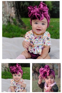 Close-up of baby girl wearing a large velvet bow headband in deep magenta on a grassy background