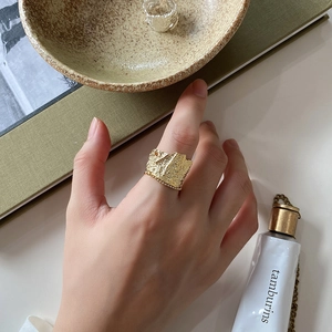 Detailed view of irregular textured gold wide ring on hand with lifestyle objects
