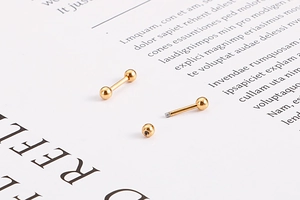 Gros plan de boucles d'oreilles haltères dorées avec détails de filetage à bille