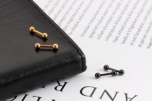 Détail de boucles d'oreilles boules vissées dorées et noires sur une surface en cuir