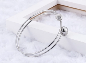 Close-up of a silver double-layered steel bangle featuring a paved crystal ball and plain sphere