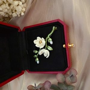 Close-up of vintage enamel camellia brooch with freshwater pearls in a red jewelry box