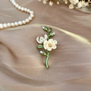 Detail of camellia enamel brooch with freshwater pearl on champagne silk background