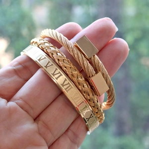 Close-up of golden Roman numeral bangle with twisted cable and woven stacking bracelets