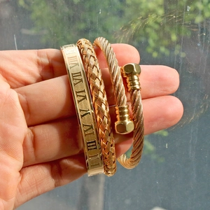 Close-up of golden Roman numeral engraved bangle and braided cable cuff bracelet set