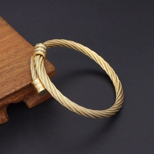 Vue détaillée du bracelet en fil d'acier doré torsadé sur un support en bois foncé